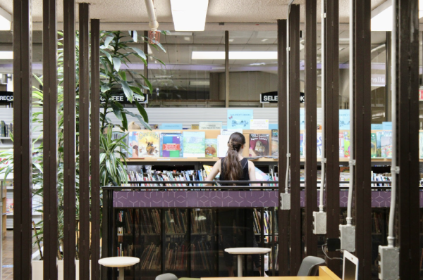 A woman chooses a book amidst the library’s many bookshelves.